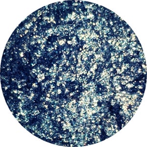 May include: A round, blue eyeshadow with a shimmery finish. The eyeshadow is made of finely milled powder and has a smooth, silky texture.