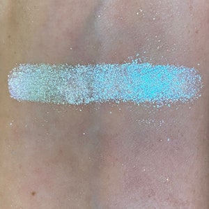 May include: A swatch of iridescent light blue glitter eyeshadow with a white base.