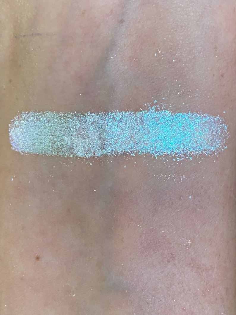 May include: A swatch of iridescent light blue glitter eyeshadow with a white base.