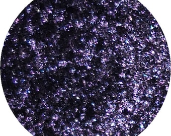 May include: A round, dark purple eyeshadow with a shimmery finish. The eyeshadow is in a compact pan.