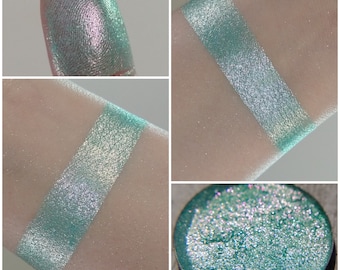 May include: A close-up of a teal green eyeshadow with a silver shimmer. The eyeshadow is shown in a pan, on a finger, and swatched on skin.