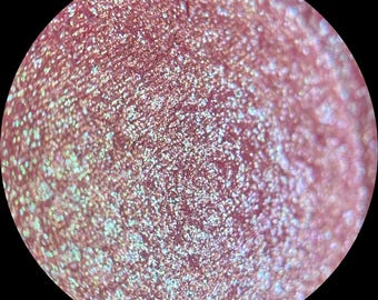 May include: Close-up of a pink eyeshadow with a shimmery, iridescent finish. The eyeshadow has a fine, glittery texture.