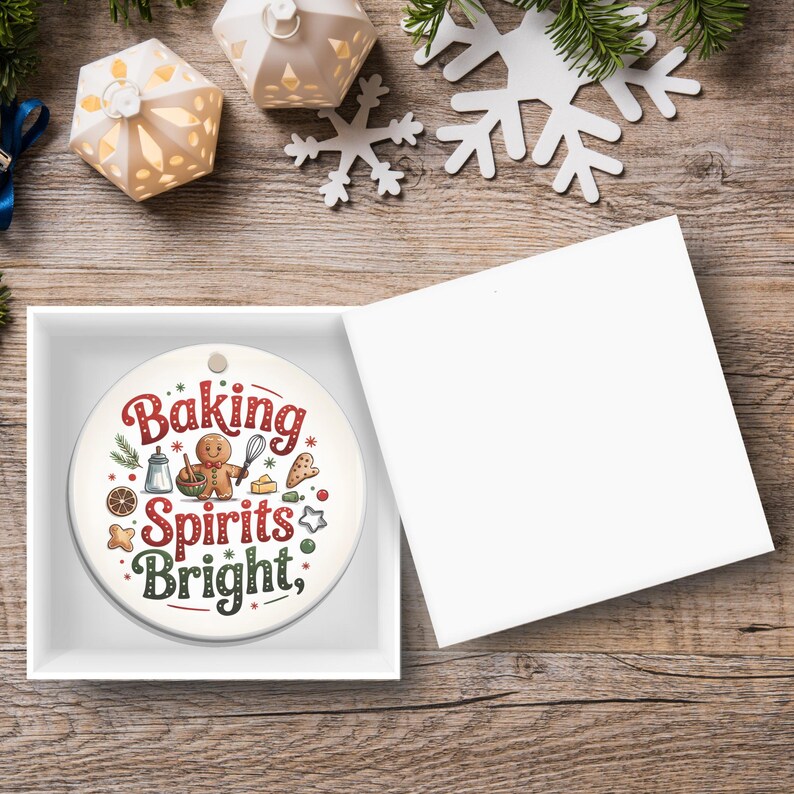 May include: A round, white Christmas ornament with the text "Baking Spirits Bright" in red and green, featuring gingerbread man and baking-themed illustrations. The ornament is in a white gift box, with a wooden background.
