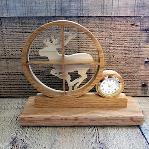 May include: A wooden clock with a deer silhouette design. The clock is mounted on a wooden base and has a round face with black numbers.