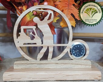 May include: A wooden golf themed clock with a golfer silhouette, golf cart, and clock face. The clock is on a wooden base and has the text "FromTheWoodpile.com Custom Handcrafted Woodwork and Vinyl Designs" on the side.