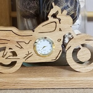 May include: Wooden motorcycle clock with a round clock face and gold trim. The motorcycle is on a wooden base.
