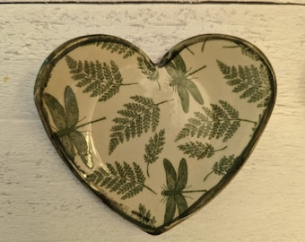 Puede incluir: Un plato de cerámica en forma de corazón con fondo blanco y un patrón verde de helechos y libélulas.