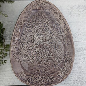 May include: A large, oval-shaped serving platter with a raised, intricate, paisley-like design. The platter is a light purple color.