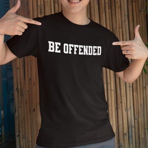 Op de afbeelding: Zwart T-shirt met witte tekst die "BE OFFENDED" zegt.