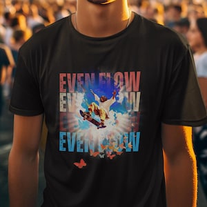 Op de afbeelding: Een zwart T-shirt met een afbeelding van een persoon die skateboardt in de wolken. De afbeelding bevat de tekst "EVEN FLOW" die drie keer wordt herhaald in verschillende kleuren.