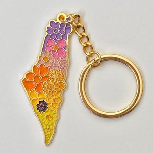 May include: A gold-coloured keychain with a floral design in the shape of a country. The flowers are in shades of purple, pink, orange, and yellow. The keychain has a gold chain and a round key ring.