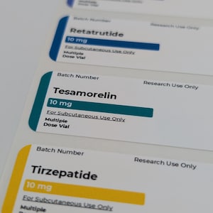 Pode incluir: Close-up de várias etiquetas brancas com detalhes azuis, verde-azulado e amarelos. Cada etiqueta exibe o nome de um medicamento, sua dosagem (10 mg) e instruções para uso subcutâneo. O texto "Multiple Dose Vial" também está presente.