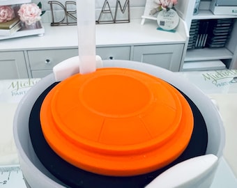 May include: A white and gray tumbler with an orange lid and a clear straw. The tumbler has a black interior and a white handle. The image is taken from a high angle, showing the top of the tumbler.