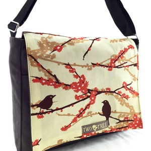 May include: A brown canvas messenger bag with a cream-colored flap featuring a floral pattern with red blossoms and two black birds. The flap has the text "TWO TREE" in brown.