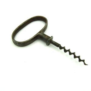 Könnte beinhalten: Antiker Korkenzieher aus Metall mit dunklem, gealtertem Aussehen. Der Korkenzieher hat eine Wendel und einen ovalen Griff. Griff und Wendel sind durch ein kleines, kreisförmiges Teil verbunden. Das Werkzeug dient zum Entfernen von Korken aus Flaschen.