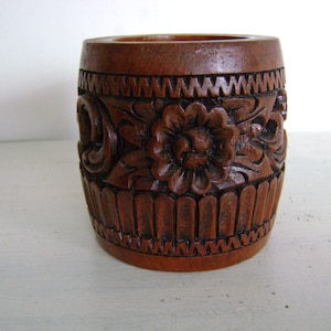 Könnte beinhalten: Ein brauner Holzbehälter mit aufwendigen Schnitzereien von Blumen und Blättern. Der Behälter hat eine zylindrische Form und eine glatte, polierte Oberfläche.