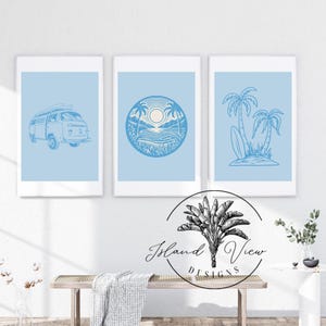 Peut inclure: Trois illustrations bleues et blanches sur un fond blanc. Les illustrations représentent un van vintage, une scène de plage avec un palmier et un soleil, et deux palmiers avec une planche de surf. Le texte "Island View Designs" est en lettres noires sous les illustrations.