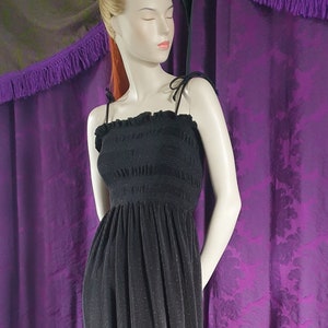 Puede incluir: Un vestido maxi negro con detalles dorados. El vestido tiene un corpiño fruncido y una falda fluida. El vestido está en un maniquí.