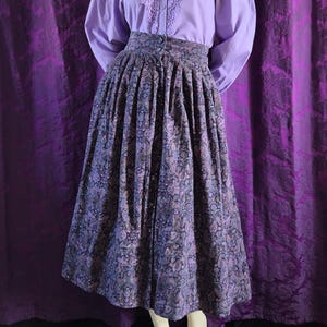 May include: A vintage two-piece outfit on a mannequin. The ensemble features a lavender blouse with a lace-trimmed collar and button-down front. The skirt is a midi length with a paisley pattern in shades of purple, blue, and brown.