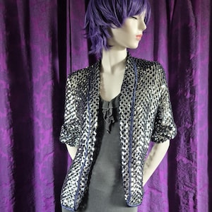 May include: A mannequin wearing a gray dress with a ruffled hem and a sequined jacket. The jacket is silver and black with blue trim. The mannequin has purple hair and is posed in front of a purple curtain.