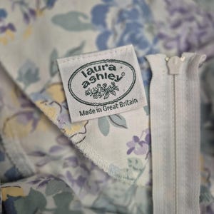 May include: Close-up of a floral fabric with a white zip. The fabric displays a pattern of blue, purple, and yellow flowers on a light background. A label reads "laura ashley Made in Great Britain."