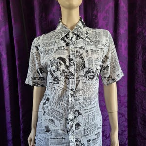 May include: White button-up shirt with a black newspaper print design. The short-sleeved shirt features a collared neckline and two chest pockets. The print includes various images and text, creating a vintage aesthetic.