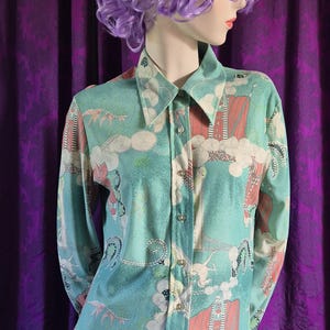 May include: A long-sleeved button-down shirt in a teal color with a unique pattern featuring clouds, buildings, and floral elements in pink, white, and cream. The shirt has a classic collar and buttoned cuffs.