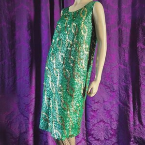 May include: A sleeveless green sequin dress with gold and silver accents. The dress is knee-length and has a simple design. The dress is displayed on a mannequin.