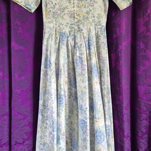 May include: A vintage floral print dress with short sleeves. The dress has a light background with blue, yellow, and purple floral patterns. It has a fitted bodice and a flowing skirt, with a zip closure down the front.