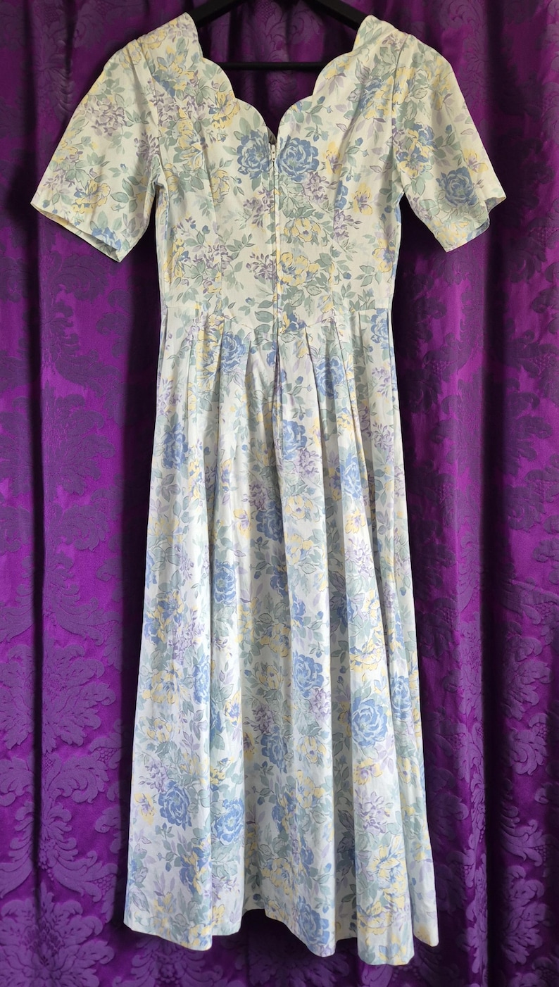 May include: A vintage floral print dress with short sleeves. The dress has a light background with blue, yellow, and purple floral patterns. It has a fitted bodice and a flowing skirt, with a zip closure down the front.