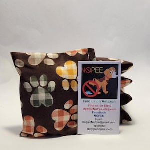 May include: A stack of brown fabric dog pee pads with a paw print pattern. The pads are labeled "NOPEE" and have a cartoon dog on them. The label also includes contact information for the company, including their website, Facebook page, and email address.