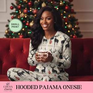 May include: Cream-colored hooded pajama onesie with a pattern of black reindeer and red Christmas trees. The pajama set includes a zip-up top and matching pants. The text "SMALL PRINT" is in a green starburst, and the text "HOODED PAJAMA ONESIE" is at the bottom.