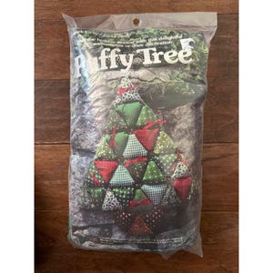May include: A clear plastic bag containing a "Puffy Tree" holiday wall hanging or door decoration kit. The tree is made of red, green, and white patterned fabric triangles. The text "Puffy Tree" is visible on the packaging.