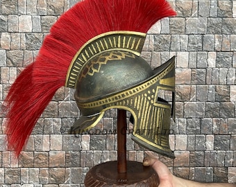 Peut inclure: Un casque spartiate en or et noir avec une plume de crin de cheval rouge sur un support en bois. Le casque est orné d'un motif détaillé avec des accents dorés.