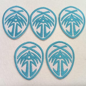 Puede incluir: Cinco parches bordados con fondo blanco y diseño turquesa. Cada parche tiene forma ovalada con un emblema turquesa que presenta un árbol estilizado y formas geométricas. Los parches están cuidadosamente dispuestos sobre una superficie blanca.