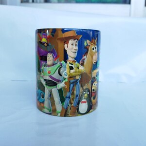 Può includere: Tazza cilindrica in ceramica con personaggi del film d'animazione "Toy Story". La tazza presenta Woody, Buzz Lightyear e altri personaggi dai colori vivaci. La tazza è adatta per bevande calde o fredde.
