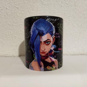 May include: Black ceramic mug with a colorful graphic of a female character with blue hair and a black and pink outfit. The background is black with colorful scribbles and text that includes "BOOM" and "VAR LIAR".