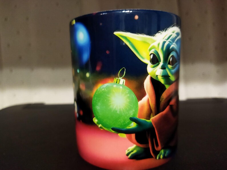 K&ouml;nnte beinhalten: Keramikbecher mit festlichem Design. Er zeigt eine gr&uuml;ne Figur, die eine gr&uuml;ne Kugel h&auml;lt. Der Becher hat einen dunkelblauen Hintergrund mit bunten Lichtern, und die Figur tr&auml;gt eine braune Robe.