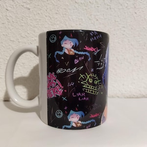 May include: A white ceramic mug with a black handle. The mug has a black and white design with colorful graffiti-style writing and cartoon characters. The writing includes the words "liar liar" and "boo!"