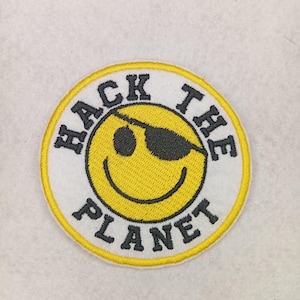 Puede incluir: Parche redondo con una carita sonriente amarilla con un parche en el ojo y gafas de sol. El fondo blanco tiene las palabras "HACK THE PLANET" en letras negras. El borde es amarillo.