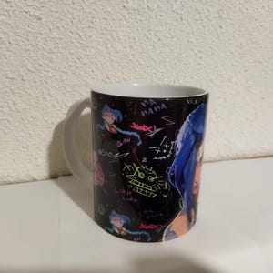 May include: A black and white ceramic mug with a colorful graphic print of a woman with blue hair and the words "Blah" and "Liar Liar" on the mug.
