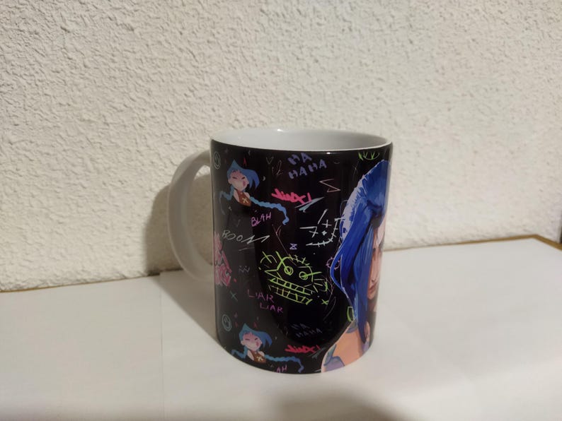 May include: A black and white ceramic mug with a colorful graphic print of a woman with blue hair and the words "Blah" and "Liar Liar" on the mug.