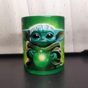 Pu&ograve; includere: Tazza in ceramica verde con un'immagine a cartoni animati di Grogu, noto anche come Baby Yoda, che tiene in mano un ornamento natalizio verde. La tazza ha uno sfondo verde ed &egrave; probabilmente un prodotto a tema Star Wars.