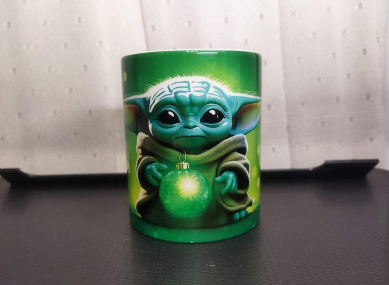 Pu&ograve; includere: Tazza in ceramica verde con un'immagine a cartoni animati di Grogu, noto anche come Baby Yoda, che tiene in mano un ornamento natalizio verde. La tazza ha uno sfondo verde ed &egrave; probabilmente un prodotto a tema Star Wars.