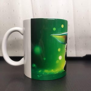 Pu&ograve; includere: Tazza in ceramica bianca con un design verde e bianco. La tazza presenta un personaggio di una popolare serie di fantascienza. Il manico &egrave; bianco e lo sfondo &egrave; un gradiente di verde con globi luminosi.