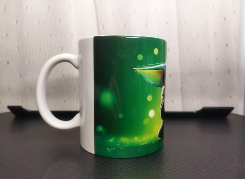 Pu&ograve; includere: Tazza in ceramica bianca con un design verde e bianco. La tazza presenta un personaggio di una popolare serie di fantascienza. Il manico &egrave; bianco e lo sfondo &egrave; un gradiente di verde con globi luminosi.