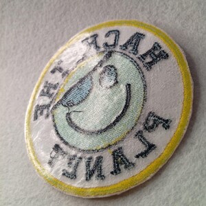 May include: An oval-shaped patch with a smiling face wearing sunglasses. The face is light green with a black outline. The patch has the text "BACK LAVA FUN" in dark blue lettering around the edge, with a yellow border.