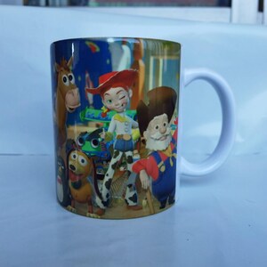 May include: White ceramic mug featuring characters from the animated film Toy Story. The mug has a white handle and is decorated with images of Woody, Jessie, Buzz Lightyear, and other characters from the movie.