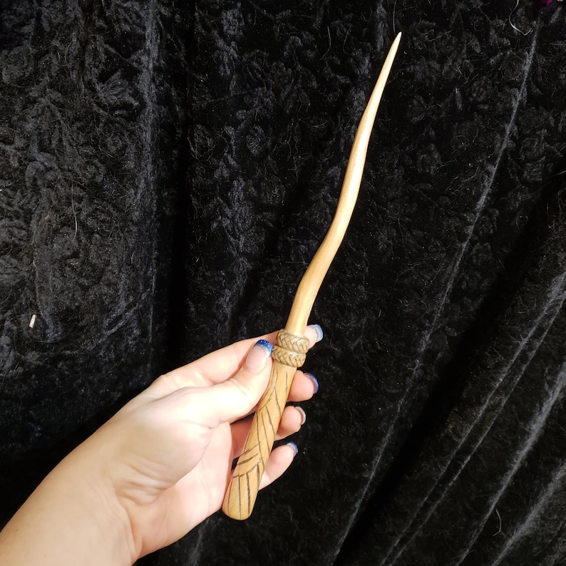 Peut inclure: Une baguette en bois avec un motif sculpt&eacute; et un enroulement en cuir brun fonc&eacute; pr&egrave;s du manche.