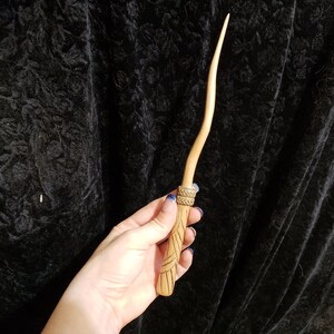 Peut inclure: Une baguette en bois avec un motif sculpt&eacute;. La baguette est de couleur brun clair et poss&egrave;de une bande brun fonc&eacute; pr&egrave;s du manche.